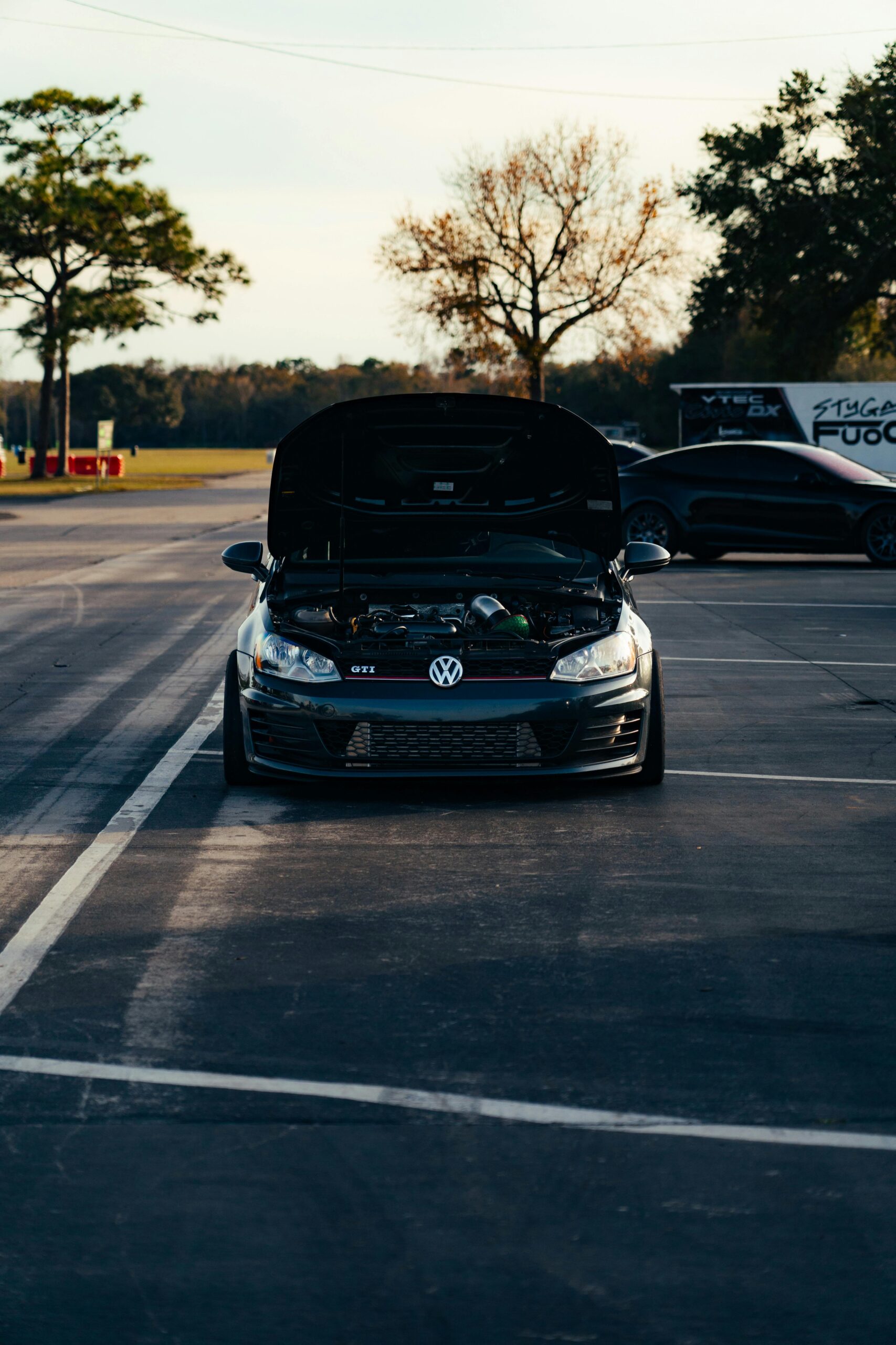 Front view of a black car with its hood up in a parking lot during the day.